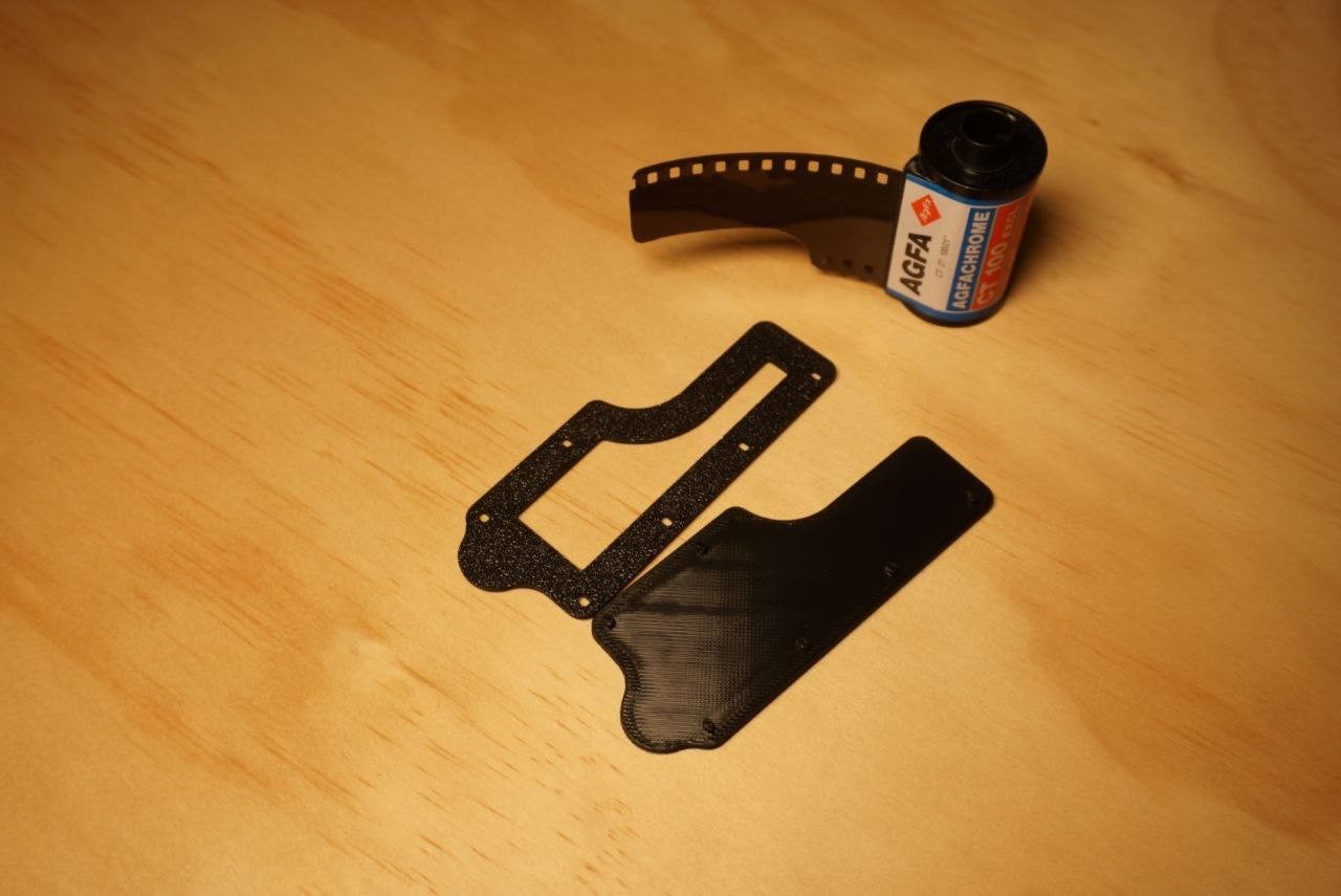 Die zwei schwarzen Teile des Filmschneiders neben einer Kleinbildpatrone auf einem Holztisch.